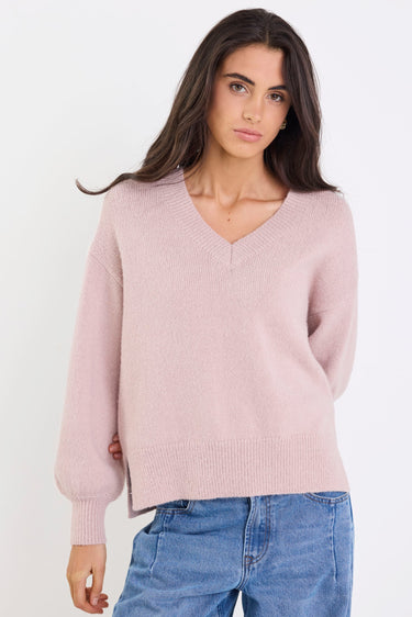 Woman wearing a pink sweater and blue jeans against a white background