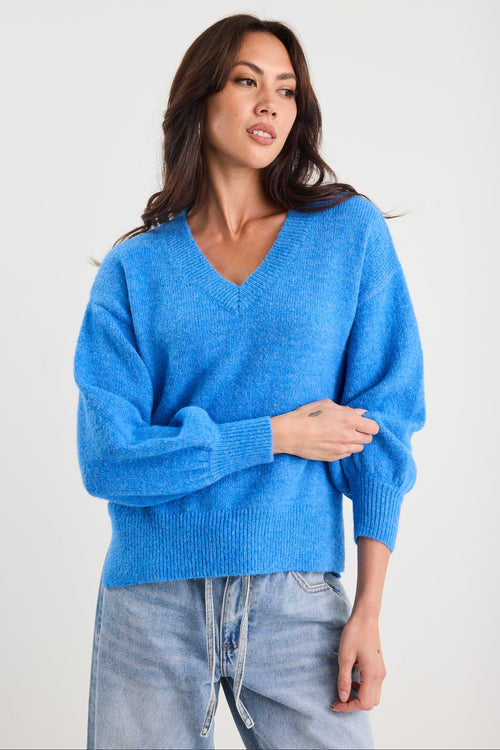Woman wearing a blue sweater and light blue jeans against a white background