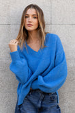 Woman wearing a blue sweater and jeans against a gray brick wall