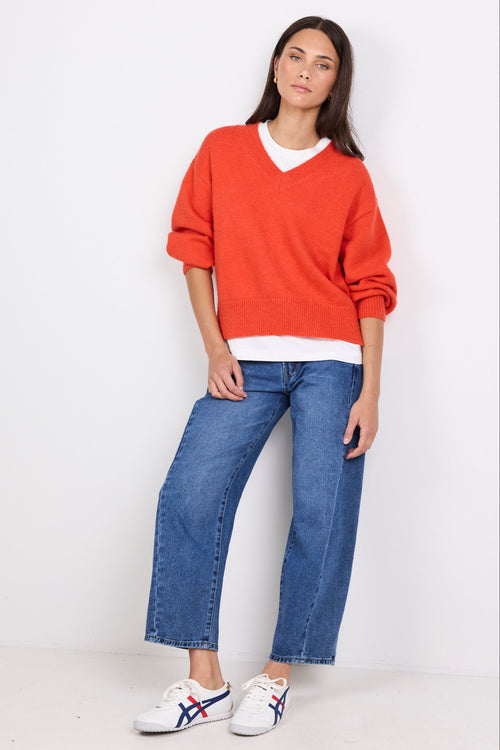 Woman wearing an orange sweater, blue jeans, and white sneakers on a white background