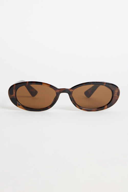Slim oval tortoiseshell sunglasses with warm brown tinted lenses, photographed on a white background