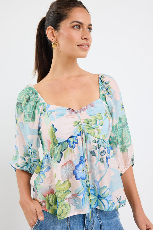 woman wearing a flowing floral puff sleeve dress with elastic waist and pastel blue and green print, styled with tan sandals.