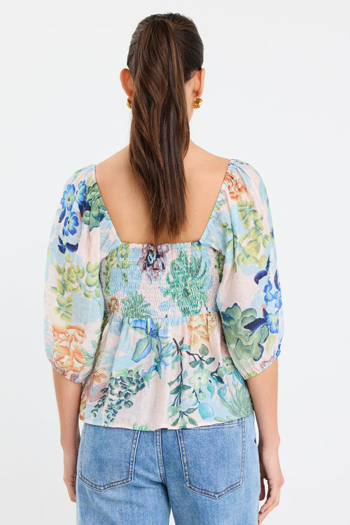 woman wearing a flowing floral puff sleeve dress with elastic waist and pastel blue and green print, styled with tan sandals.