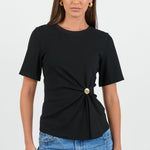 Woman wearing a black top with a gold button and blue jeans on a white background