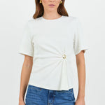 Woman wearing a white t-shirt with a twist and clasp detail and blue jeans on a white background