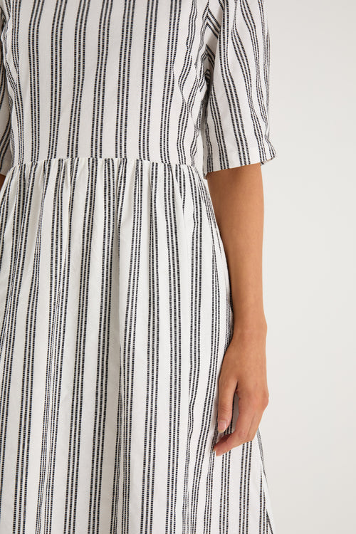 The model wears a white with black stripe detail and black sandals