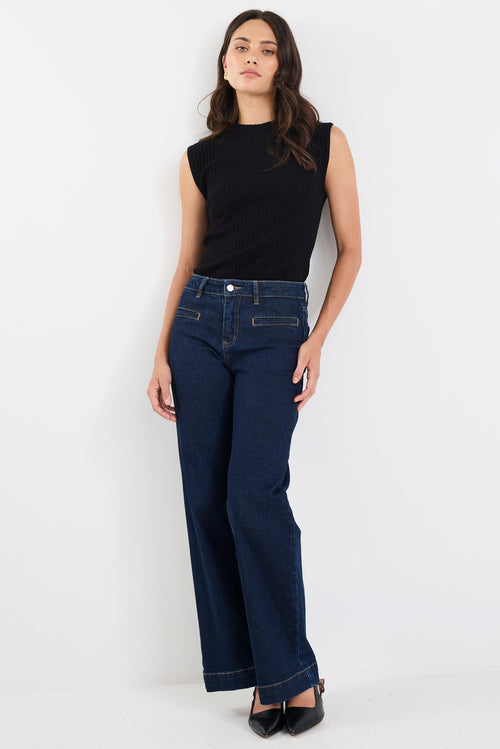 Woman wearing a black sleeveless top and dark blue jeans on a white background
