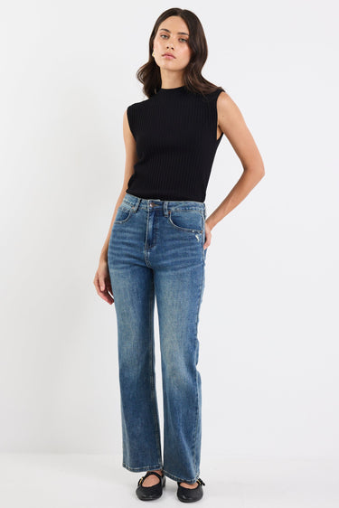 Woman wearing a black sleeveless top and blue jeans on a white background