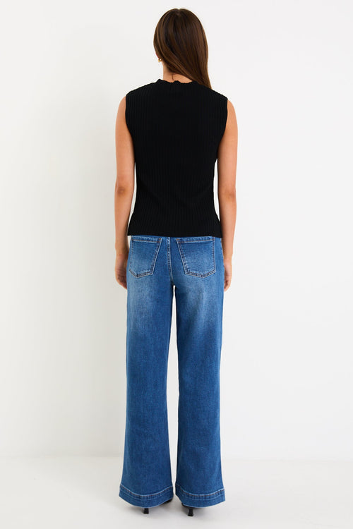 Person wearing a black sleeveless top and blue jeans on a white background