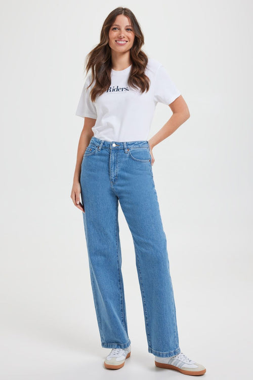 Woman wears high-rise blue wide-leg jeans with a fitted waist and relaxed leg, styled with a white graphic tee and white sneakers. The look is casual, fresh, and flattering.