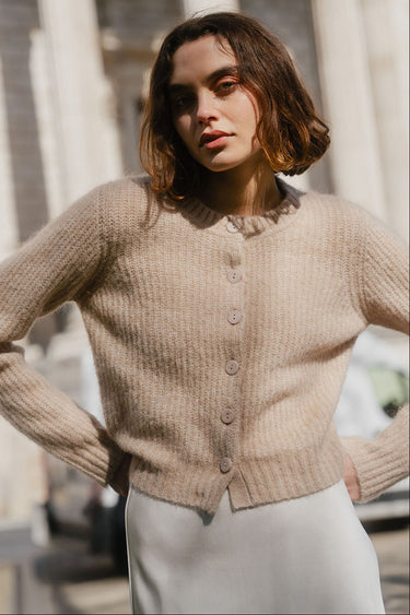 Woman wearing a beige cardigan standing outdoors with classical architecture in the background