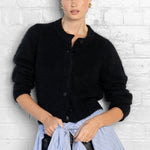 Woman wearing a black cardigan over a blue shirt against a white brick wall