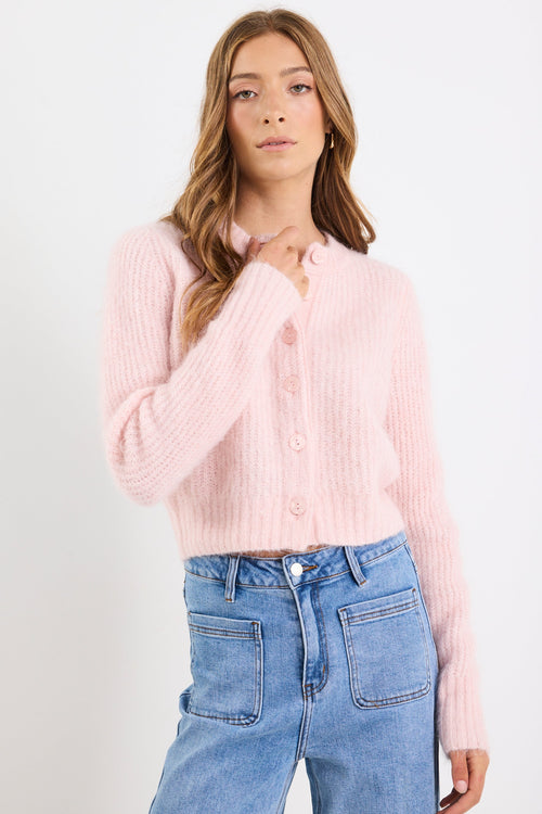 Woman wearing a light pink ribbed blouse and blue jeans on a white background
