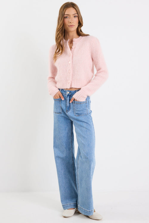 Woman wearing a light pink cardigan and blue jeans on a white background