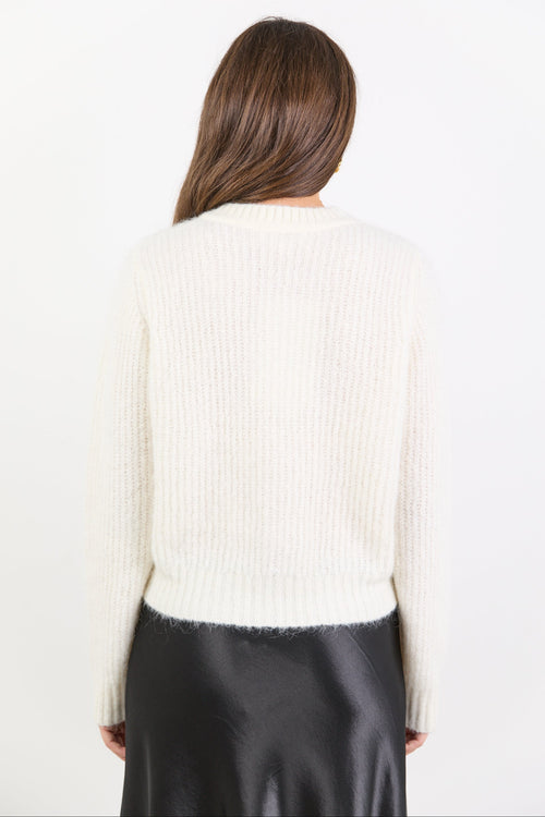 Person wearing a white ribbed sweater and black pants on a plain background