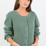 Woman wearing a green knitted cardigan and blue jeans on a white background