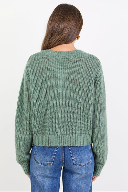 Person wearing a green sweater and blue jeans on a white background