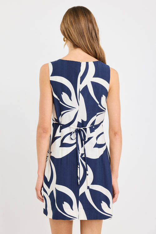 Woman wearing a navy sleeveless mini dress with a bold cream abstract print, styled simply with natural makeup and soft waves.