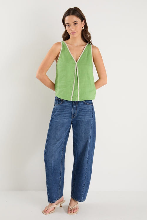 the model wears a green v-neck tank top with dark blue jeans