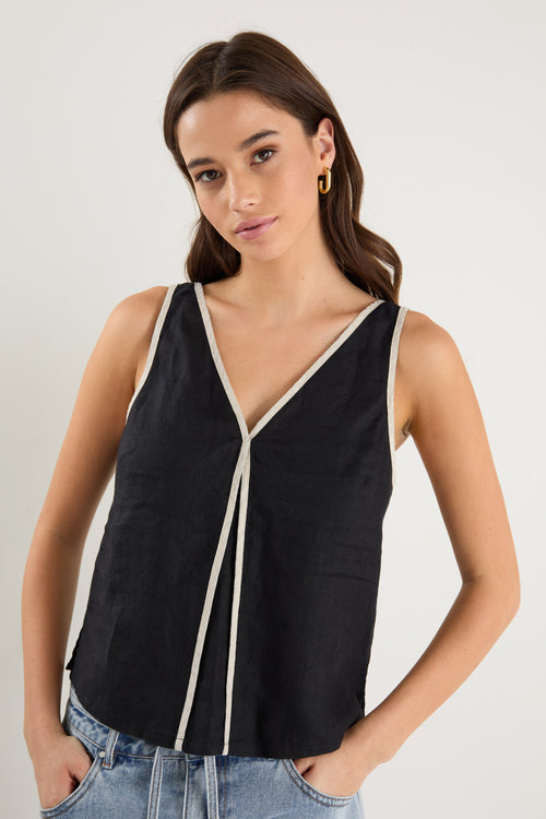 Woman wearing a sleeveless black linen top with contrast beige trim, styled with relaxed mid-blue denim jeans.