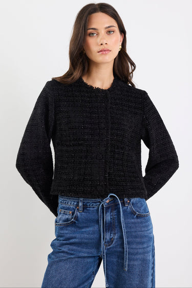 Woman wearing a black textured sweater and blue jeans on a white background