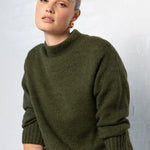 Woman wearing a green sweater sitting on a chair against a white wall