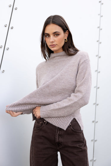 Woman wearing a gray sweater and dark jeans against a white background