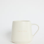 Cream-coloured ceramic mug with the words ‘Hug In A Mug’ embossed on the front, photographed on a white background