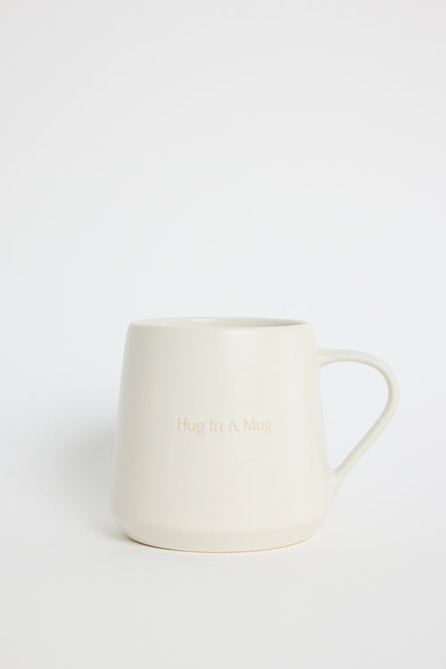 Cream-coloured ceramic mug with the words ‘Hug In A Mug’ embossed on the front, photographed on a white background