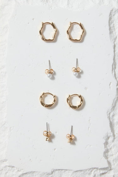 Set of gold earrings on a white stone display block against a beige background