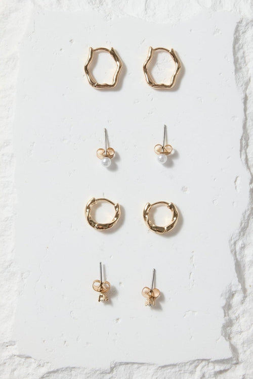 Set of gold earrings on a white stone display block against a beige background