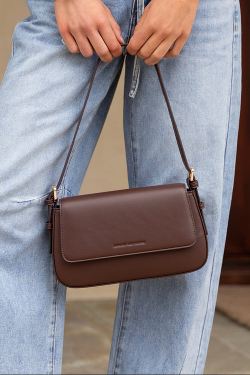 Person wearing light blue jeans and a brown handbag, with a neutral background