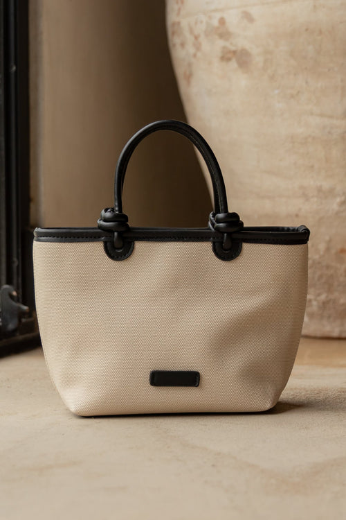 Beige handbag with black accents on a light wooden floor next to a large vase.