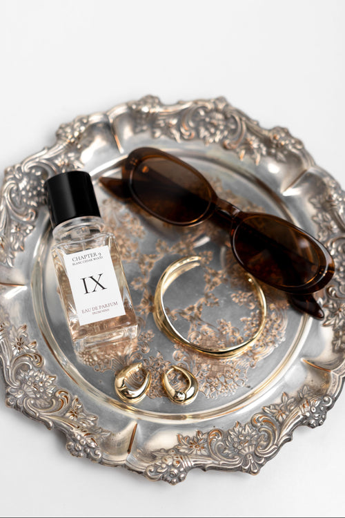 Silver tray with a bottle of perfume, sunglasses, and jewelry on a white background