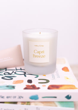 Candle labeled 'Capri Breeze' on a stack of books with a white background