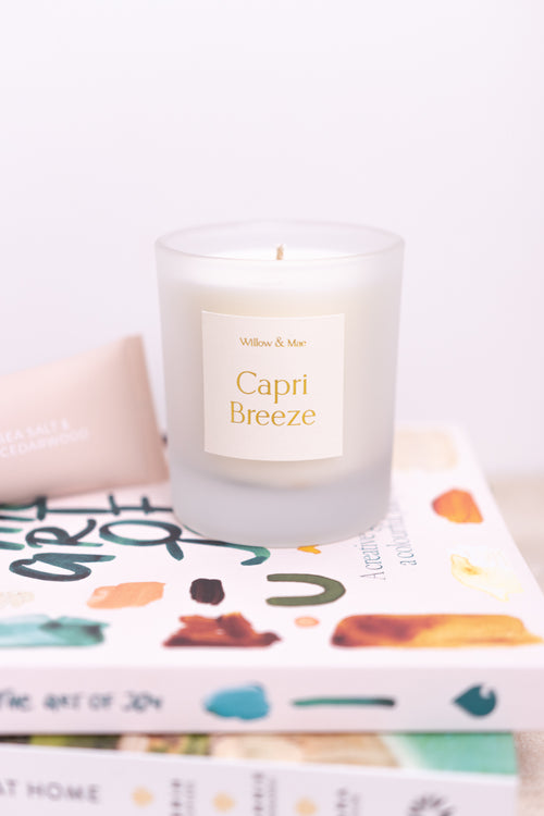 Candle labeled 'Capri Breeze' on a stack of books with a white background