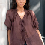 Woman wearing a brown blouse with a black door in the background