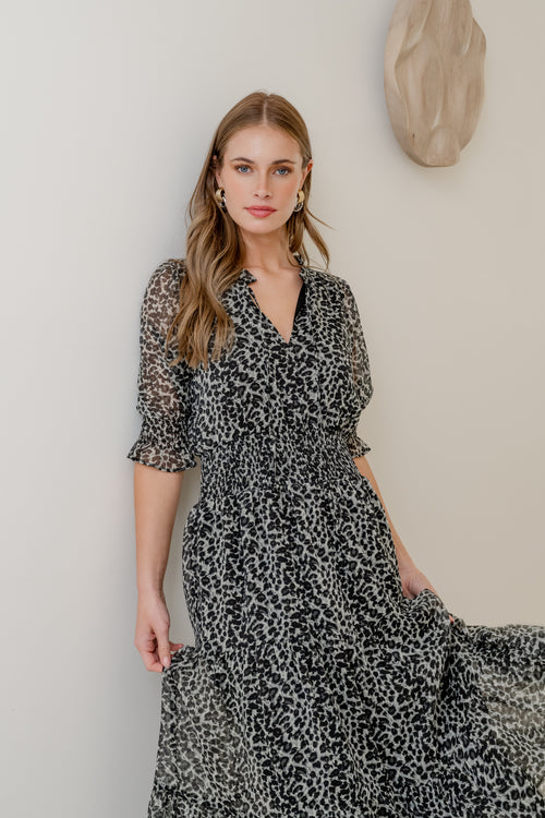 Woman wearing a black and white patterned dress against a neutral wall.