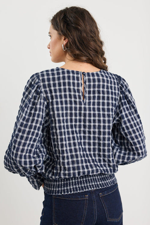 Woman wearing a blue and white checkered blouse with puffed sleeves on a plain background