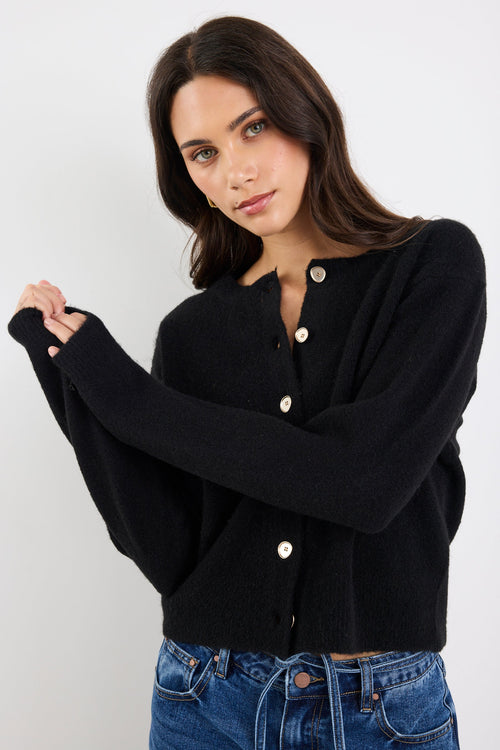Woman wearing a black cardigan with white buttons against a white background