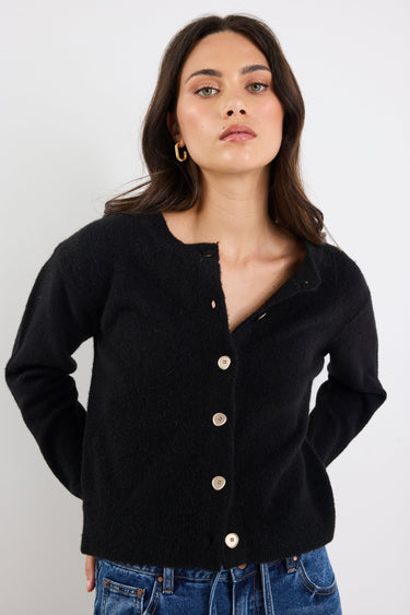 Woman wearing a black cardigan with gold buttons against a white background