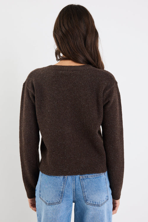 Person wearing a brown sweater and blue jeans against a white background
