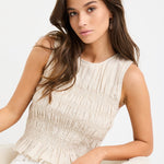 Woman wearing a natural linen sleeveless top with shirred bodice and ruffle hem, styled with ecru jeans.