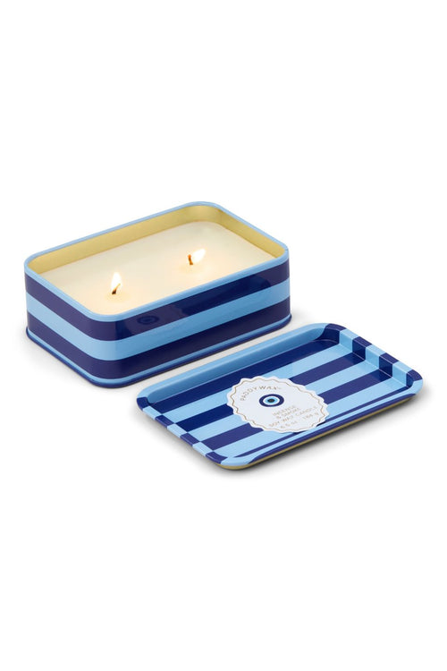 A two-wick candle in a rectangular tin with blue and light blue horizontal stripes, shown lit next to its matching lid on a white background.