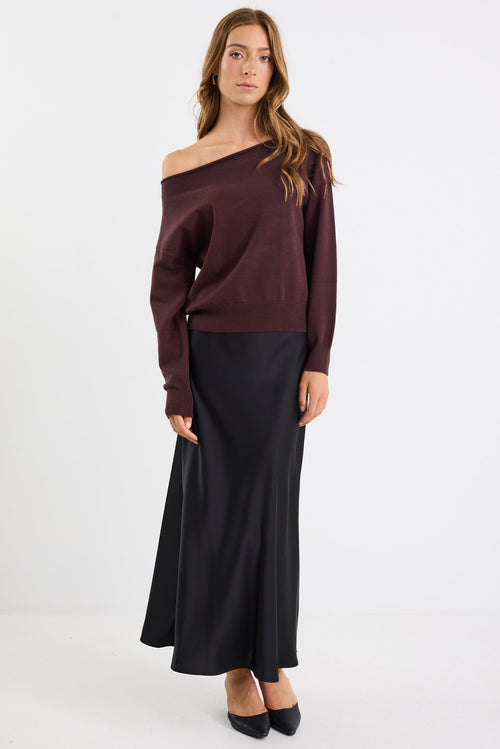 Woman wearing a brown off-shoulder sweater and black skirt on a white background