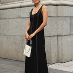 Woman wearing a black maxi dress with a square neckline and contrast stitching, styled with black heels for a chic, modern look.