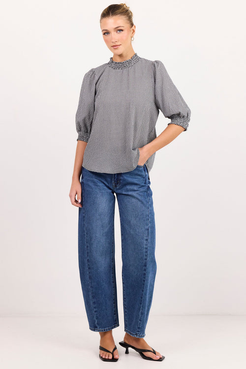 A woman modeling a gray short-sleeve blouse with a decorative embroidered neckline and puffed sleeves, paired with blue jeans and black sandals, against a plain white studio background.