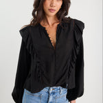 Woman wearing a black blouse with ruffled shoulders and blue jeans on a white background