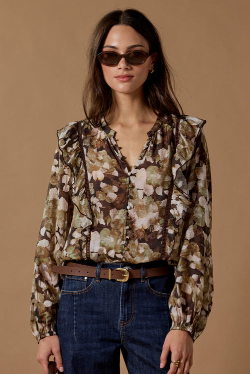 Woman wearing a floral blouse and blue jeans against a brown background
