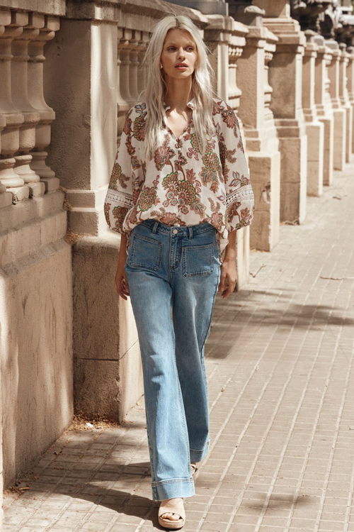 Model wears cream floral blouse and blue jeans